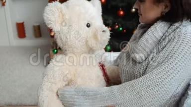 可爱的女孩坐在圣诞树旁，手里拿着一只大玩具熊